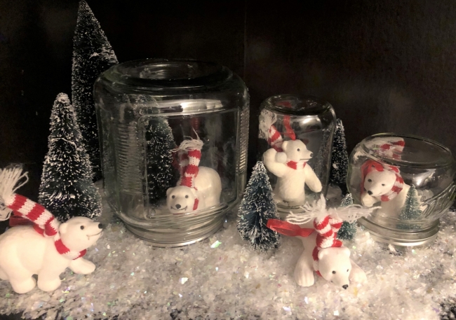 Three glass jars contain white toy bears and are set on fake snow.