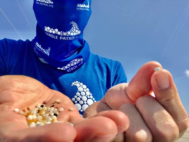 A person in blue holding out an open hand with a pile of small plastic pellets.