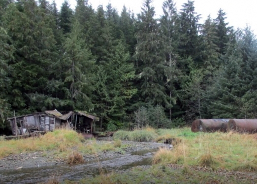 An abandoned float house and two large metal fuel containers.