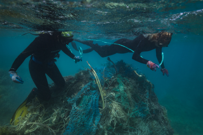Two marine debris removal technicians work to remove a net from coral.