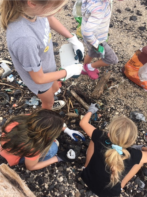 Four students pick up garbage along a beach located in Hawaii.