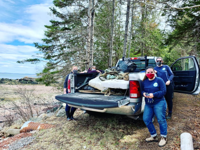 A crew next to a pickup with a bed full of debris cleaned up from a shoreline.
