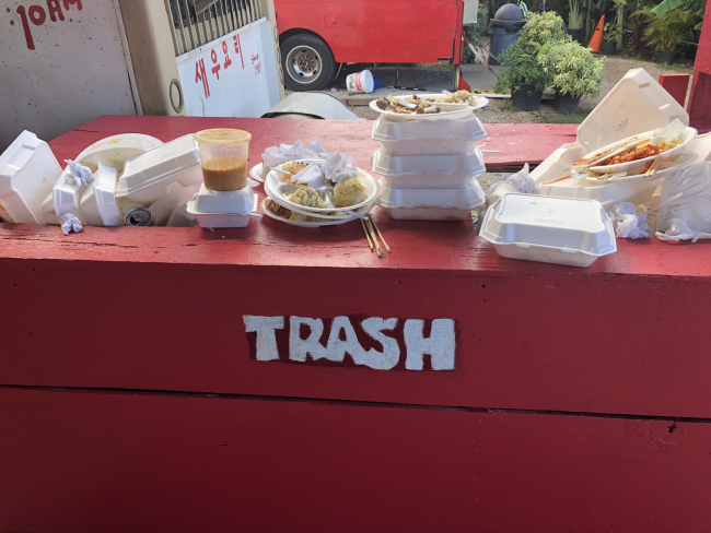 A trash receptacle overflowing with food takeout containers.
