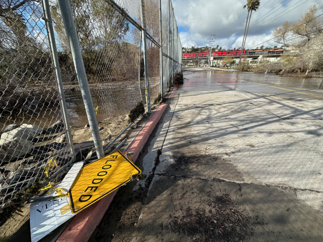 Road going over a river with a fence and downed flooded sign.