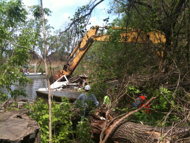 An excavator removes a derelict vessel from the water.