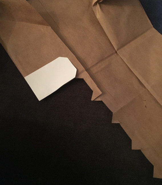 A gift tag template being used to cut gift tags from paper bags.