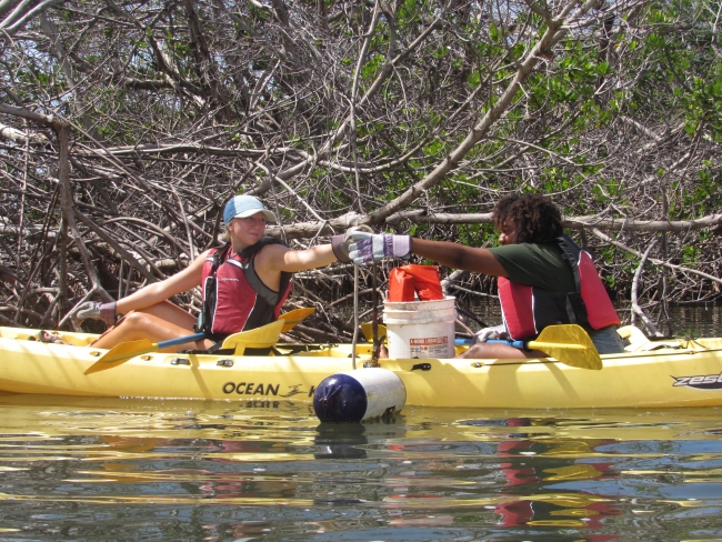 A volunteer in a kayak handing a piece of debris to another volunteer.