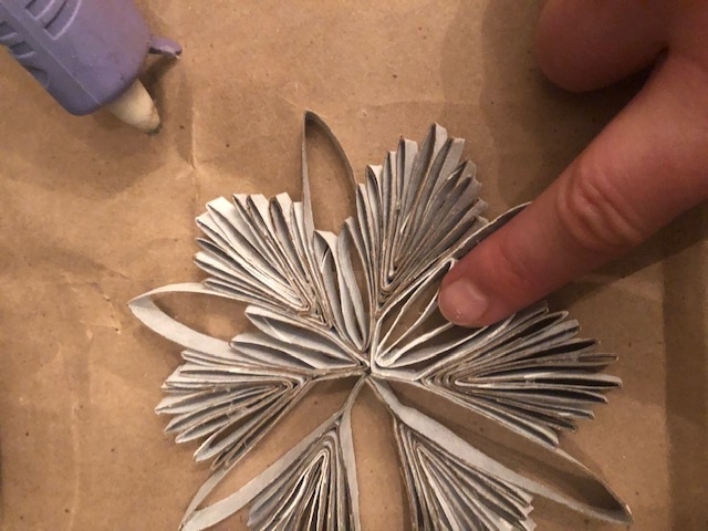 A person shapes paper towel rolls into the shape of a snowflake and glues them together with a hot glue gun.