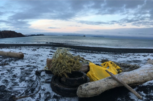 A sunset image of a shoreline in Alaska that has marine debris resting on the beach.