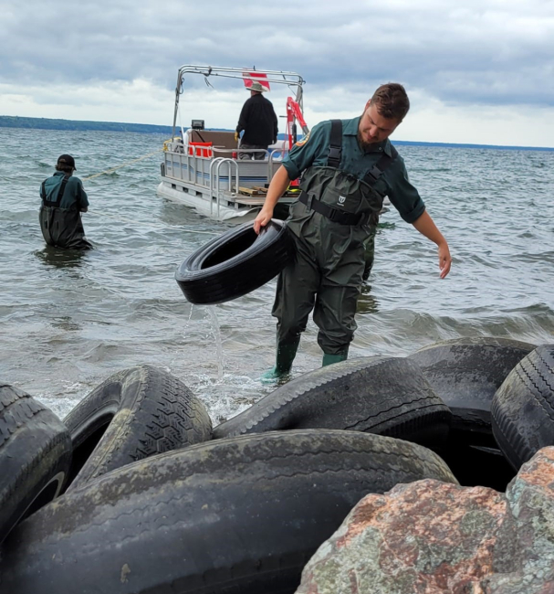 One person carrying a tire out of the water while other volunteers are on a boat and in the water.