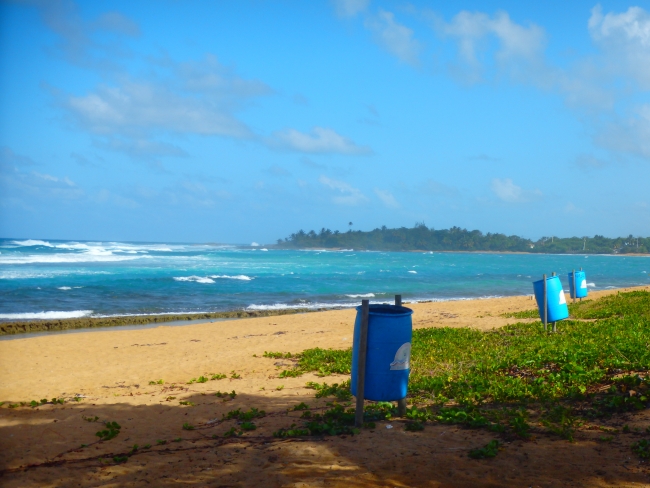 A sunny, clean Caribbean beach with trash bins.