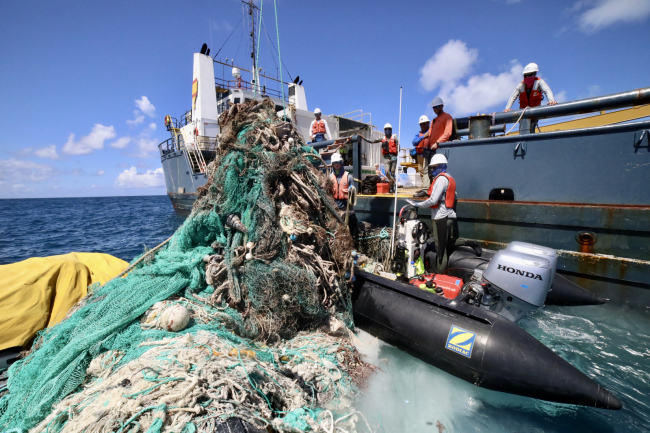 The marine debris removal team works to secure a net mass to the ship's crane.