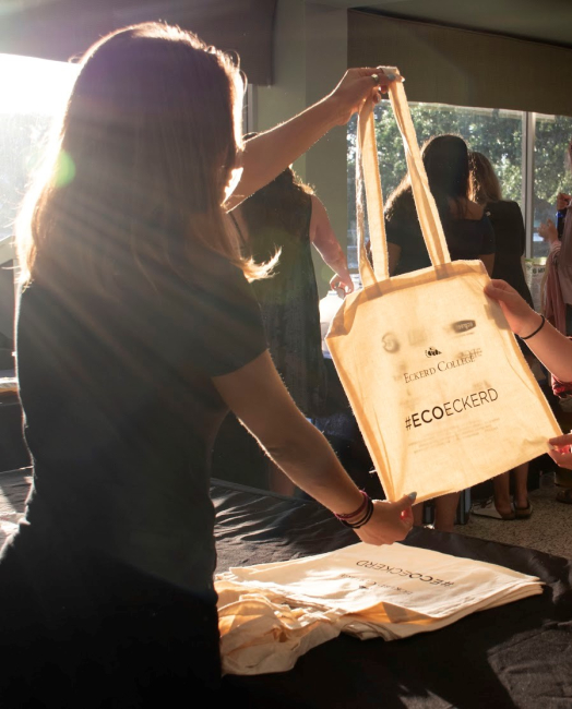 A student at an event table holding out a reusable bag.