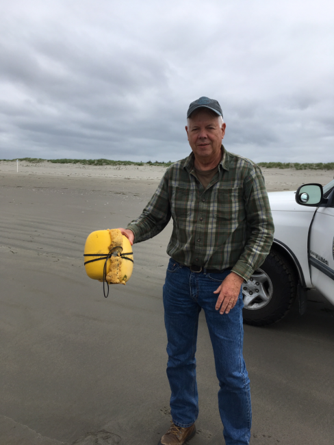 A man holds up a buoy on a beach.