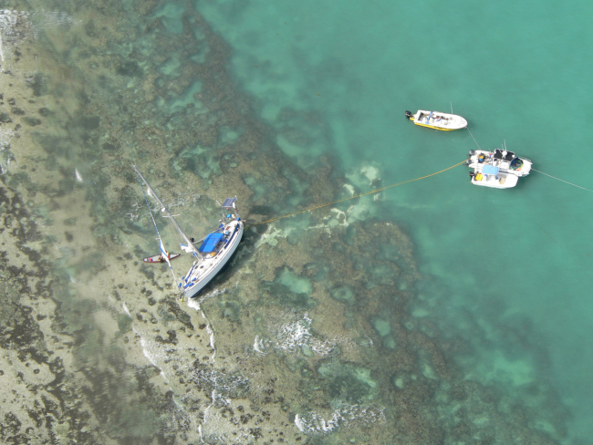 Aerial view of a sailboat grounded in shallow clear water.