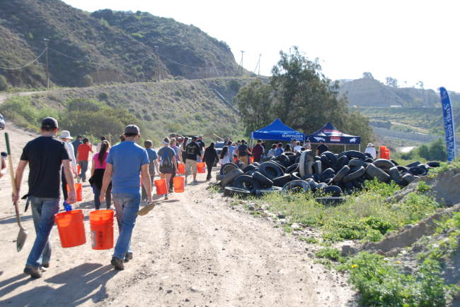 Volunteers walk down to a clean up site holding buckets and shovels. 