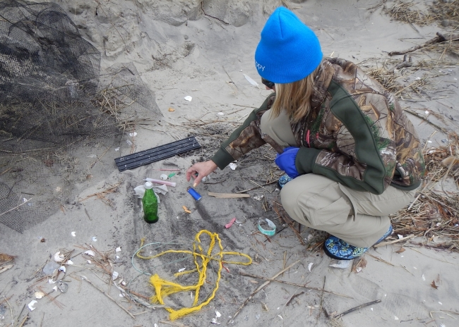 A volunteer squatting next to debris collected on a Virginia beach.