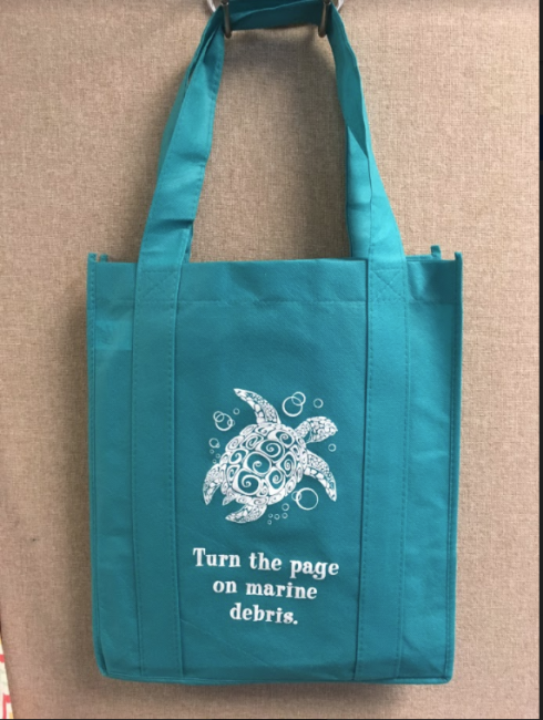 A reusable tote bag with an image of a sea turtle on it and the phrase "Turn the page on marine debris."