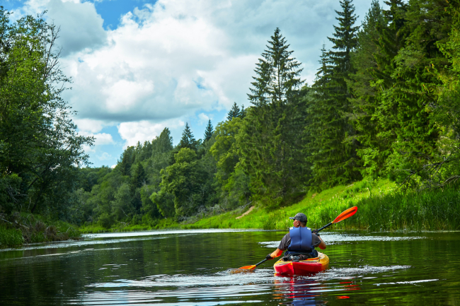 A man riding on a red kayak on a river surrounded by trees.