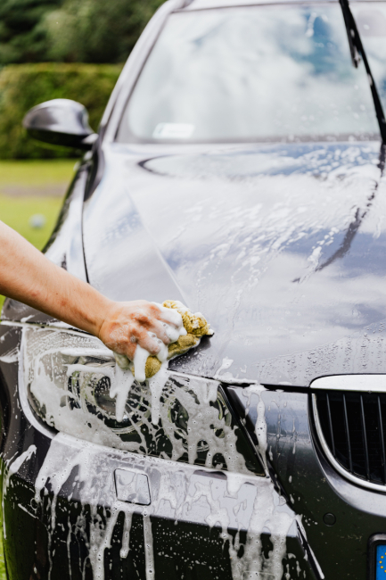 A person cleaning a car with soap and a sponge.