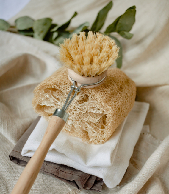 A bristle brush with a wooden handle stacked on top of a luffa sponge.