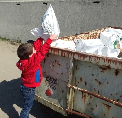 A kid throwing a bag of trash in a dumpster.