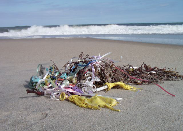 A tangle of balloon fragments and ribbon mixed with natural debris on an ocean beach.