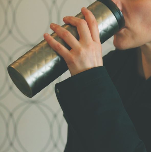 A person sipping from a reusable coffee mug.