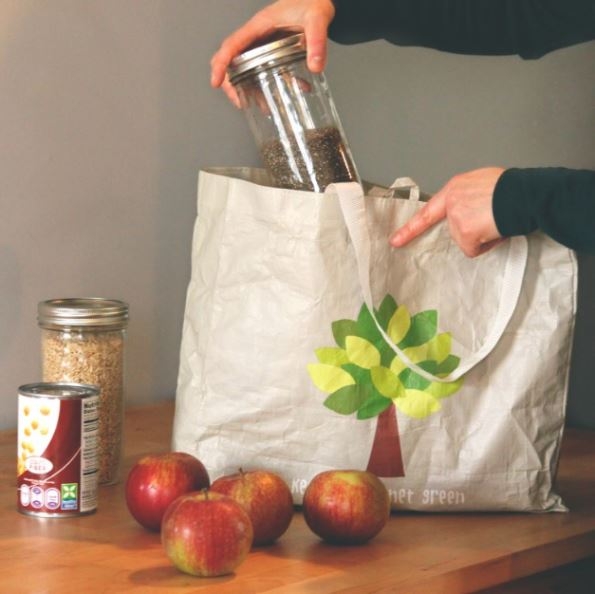 Someone pulling a glass jar of food from a reusable bag with groceries on the counter.