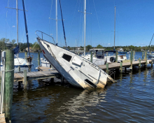 An abandoned sailboat stuck upright on the pilings of a dock.