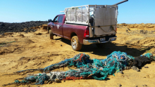 A large pick up truck and a colorful large derelict net is pictured on a beach before being hauled off.