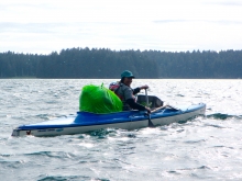 A volunteer on a kayak with a bag of debris.