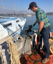 A person stands on a boat lifting up a boat anchor.