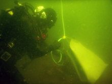 A diver in murky water holding onto a rope and lift bag.