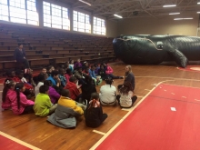 Students sit on the floor with the inflatable whale in the background.