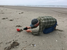 A person stoops on hands and knees to take a picture of a balloon on a beach located in Washington state.