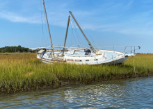An abandoned vessel grounded near the water’s edge in a marsh.