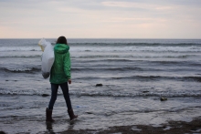 A volunteer holding a bag of collected debris walking in the water on a beach.