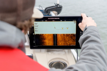 A person on a boat viewing a side-sonar screen showing crab traps on the bay floor.