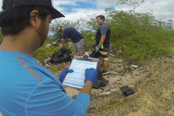 Volunteers picking up trash and recording it on a clipboard.