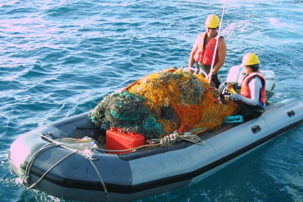 Members of a NWHI removal team ride with a boat full of collected derelict nets.